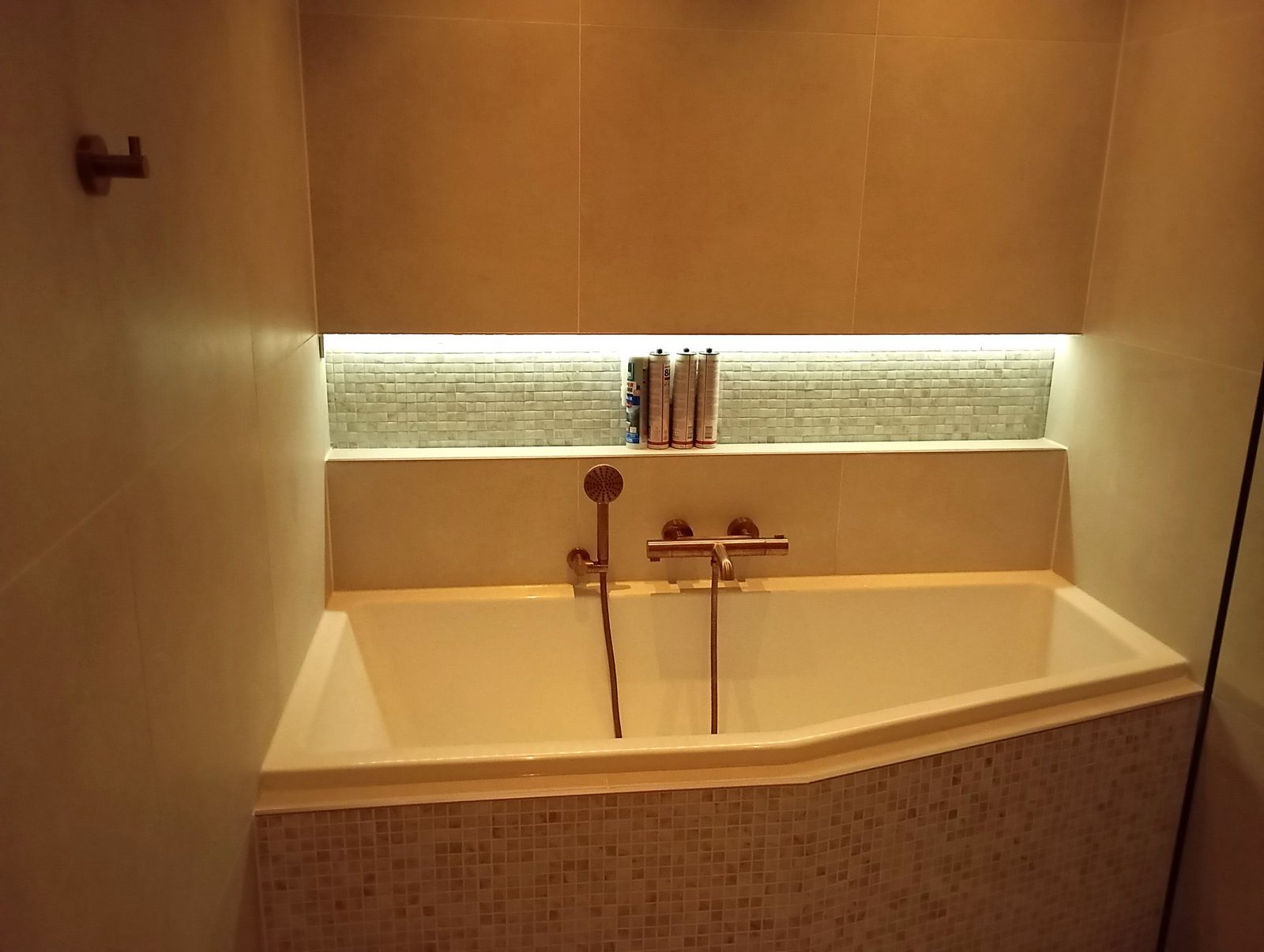 Luxe badkamer met bad en horizontale nis met ledverlichting en mozaïek, koperen kranen