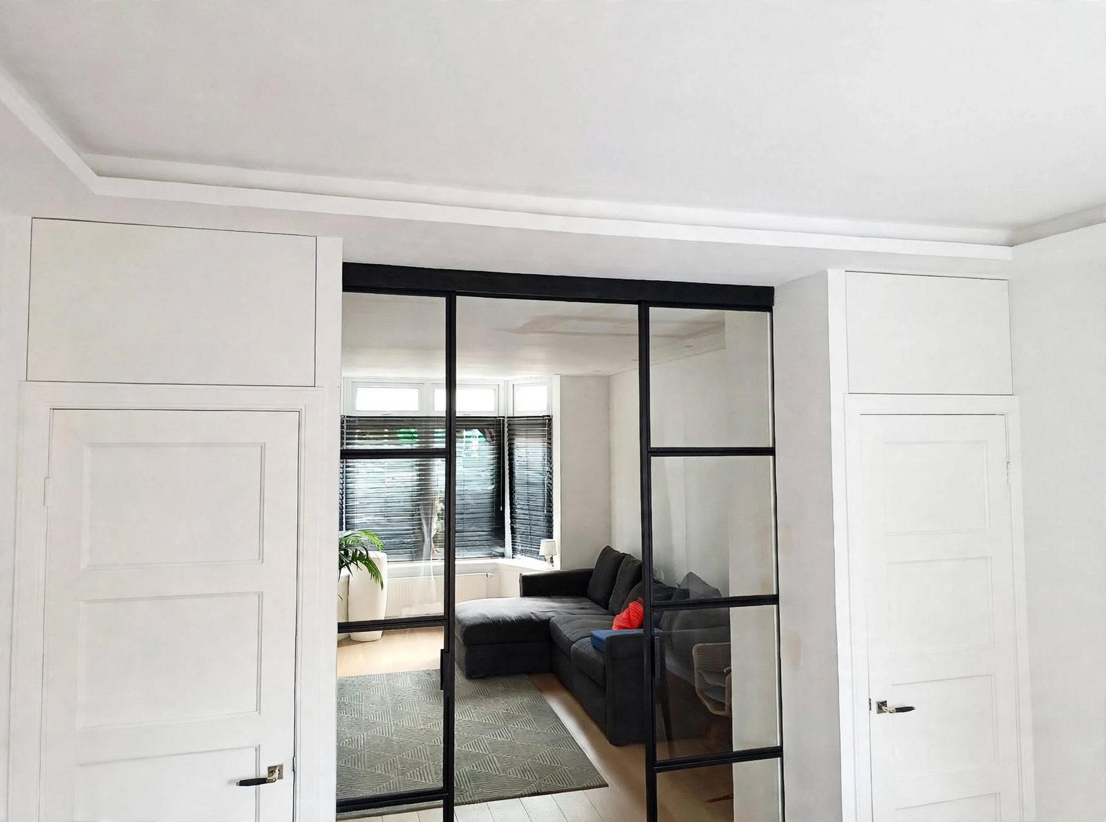 Woonkamer met een glazen schuifdeur in zwart staal in industriële stijl, tussen twee witte paneeldeuren