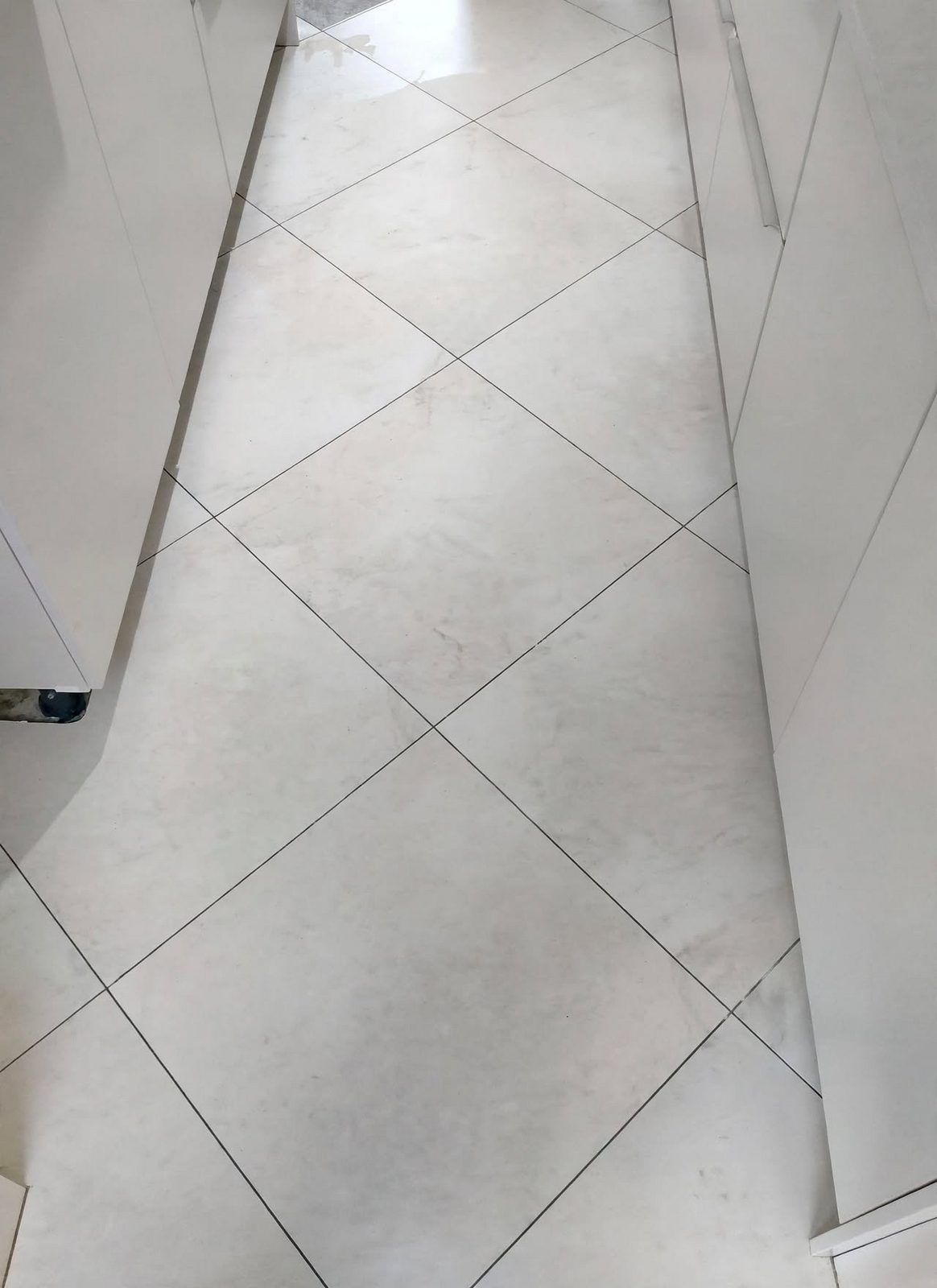 Afgewerkte keukenvloer in grootformaat tegels in marmerlook, diagonaal gelegd tussen de witte keukenkasten